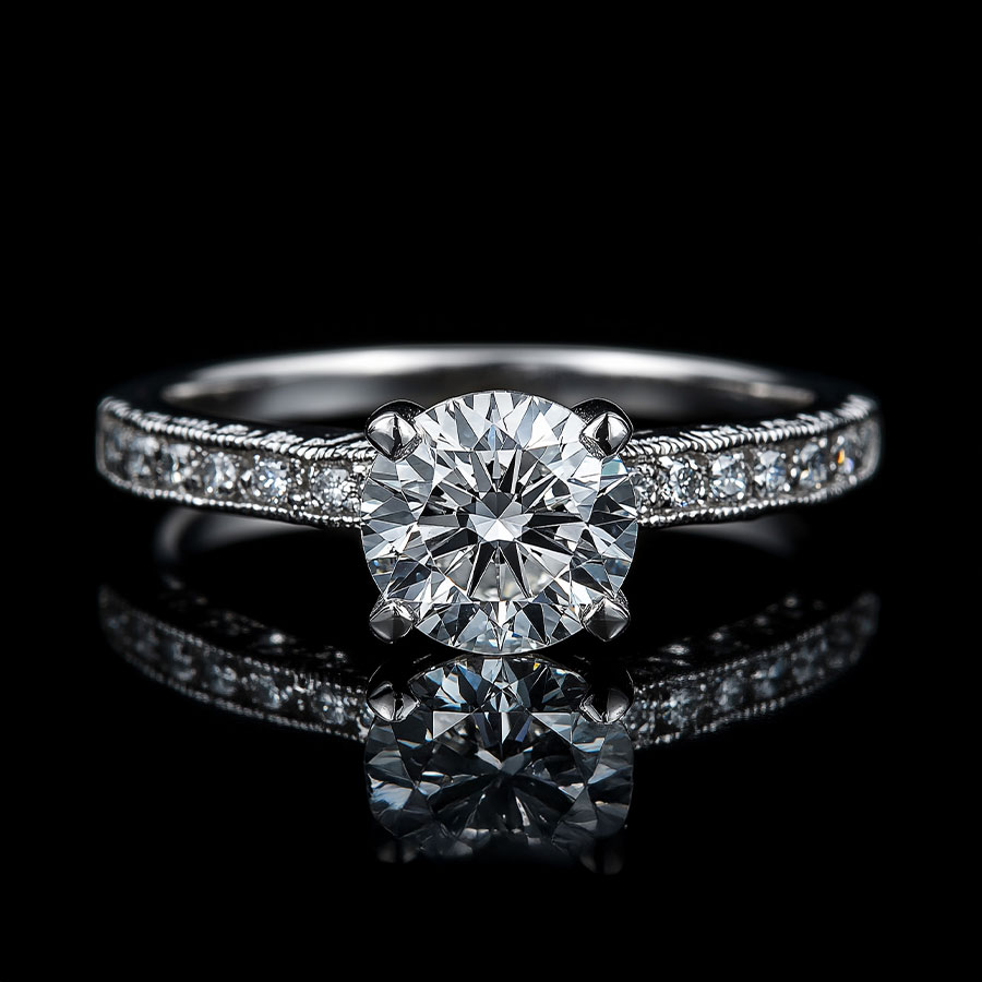 A beautiful diamond engagement ring with a large round center stone catching the light on its facets and a single row of diamonds in the shank. Front view on a dark background with a reflected surface.