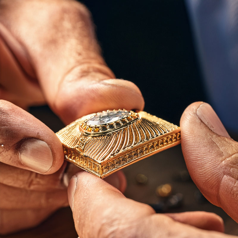 closeup of jewelers hands examining a piece of gold jewelry