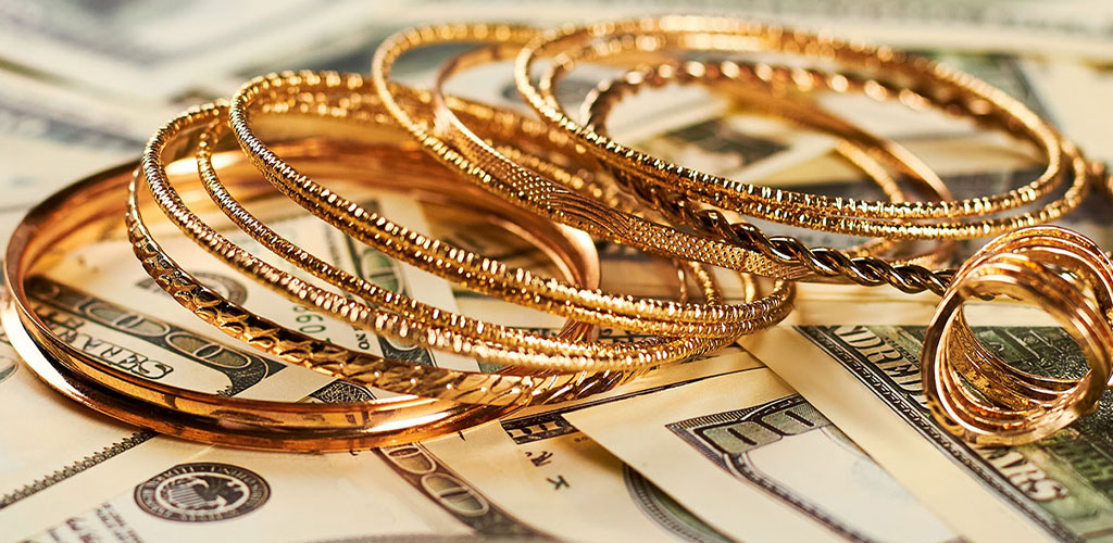 Gold jewelry sitting on hundreds of dollar bills.
