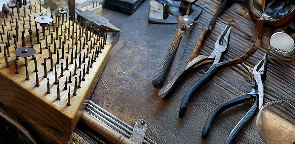 A wooden jeweler's workbench covered in files, a micrometer, a carbon block, and his work glasses.